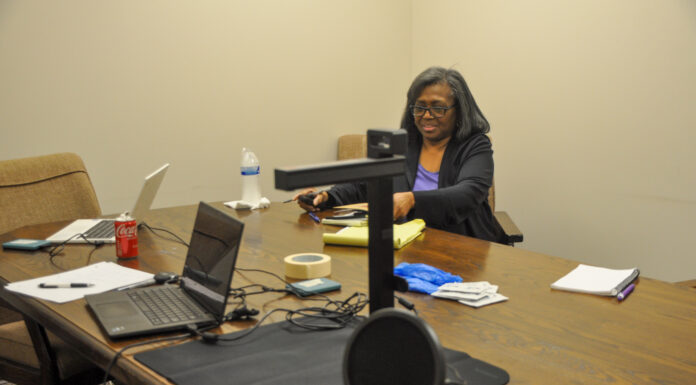 Mercer project digitally preserves history of small northeast Georgia county Person sitting at a conference table with multiple electronic devices including laptops and a microphone in a meeting room setting.