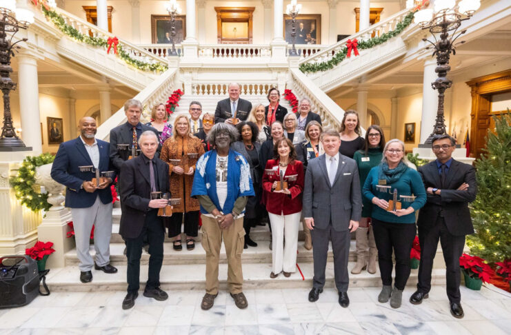 A group of people posing on a staircase in a decorated building, holding awards.