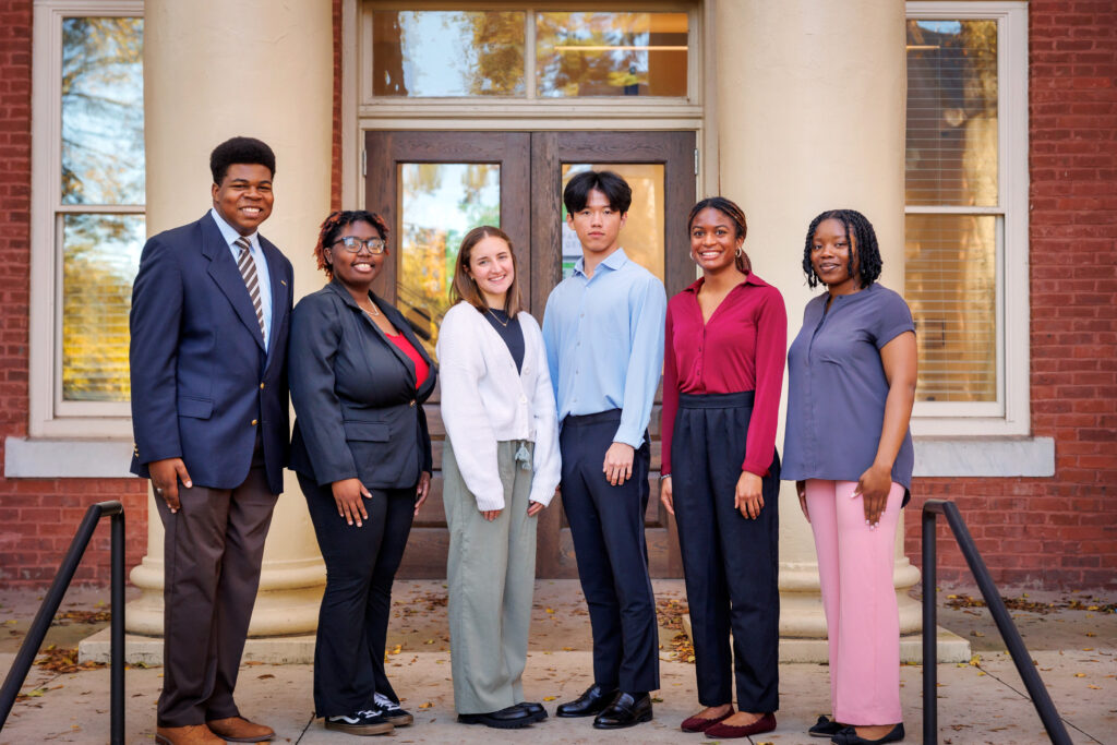 A group of six people stands in front of a building with columns, dressed in business casual attire, facing the camera.