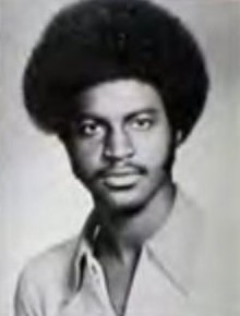 Black and white portrait of a person with an afro hairstyle and a collared shirt, facing the camera.