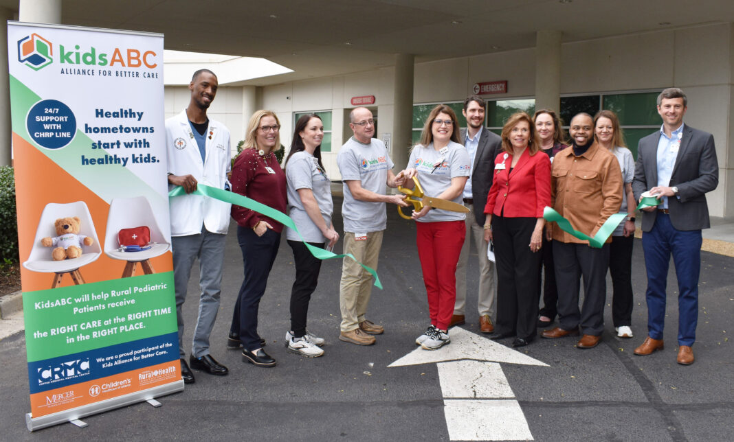 A group of people stand outside cutting a green ribbon next to a sign that reads kids ABC Alliance for Better Care.