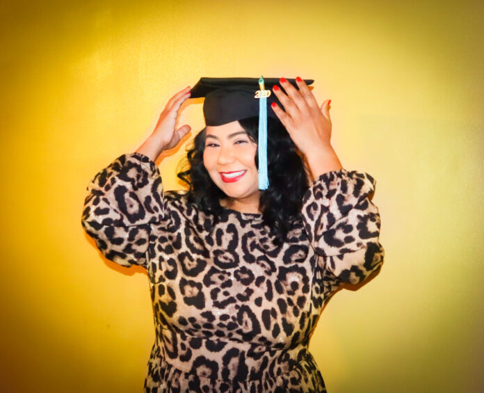 Mary Ann Santos, wearing a leopard print dress, smiles, wearing a graduation cap.