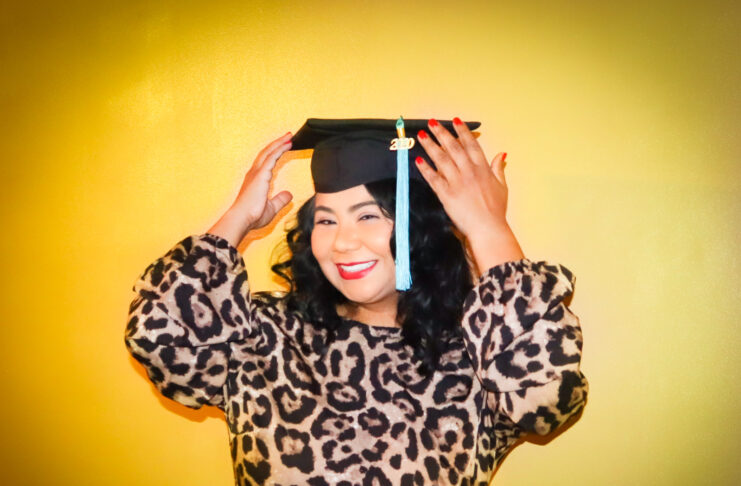 Mary Ann Santos, wearing a leopard print dress, smiles, wearing a graduation cap.