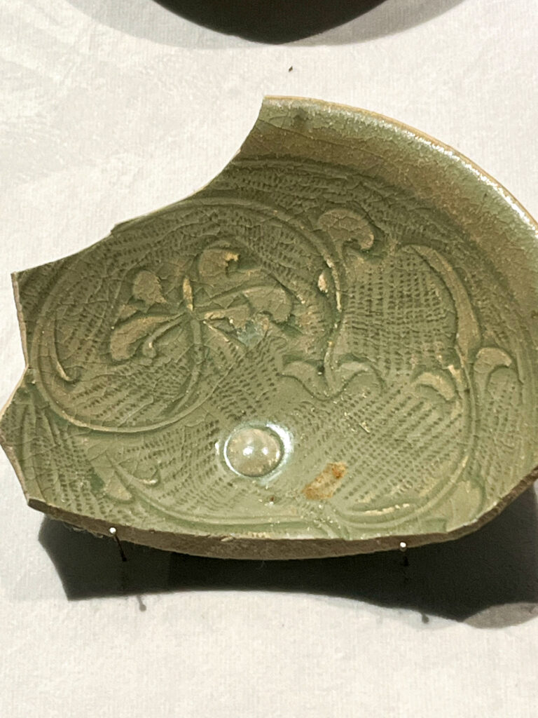 Fragment of a green, intricately textured ceramic bowl with floral patterns displayed on a white surface.