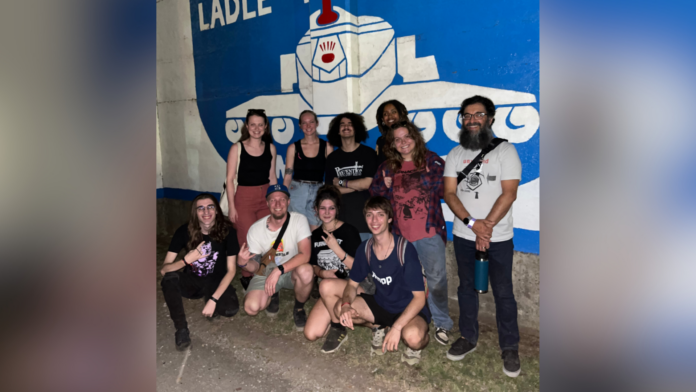 Group of people smiling in front of a mural featuring a large face.