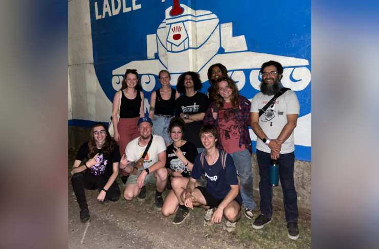 Group of people smiling in front of a mural featuring a large face.