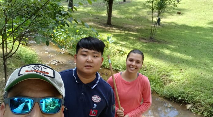 Professor’s tick and mosquito research aims to reduce occurrence of disease in humans Three people outdoors by a creek, holding nets and smiling; two standing and one wearing sunglasses in the foreground.