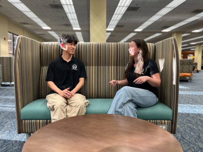 Jean Hyun and Emma Liz Soltay sit on a striped booth in Tarver Library.