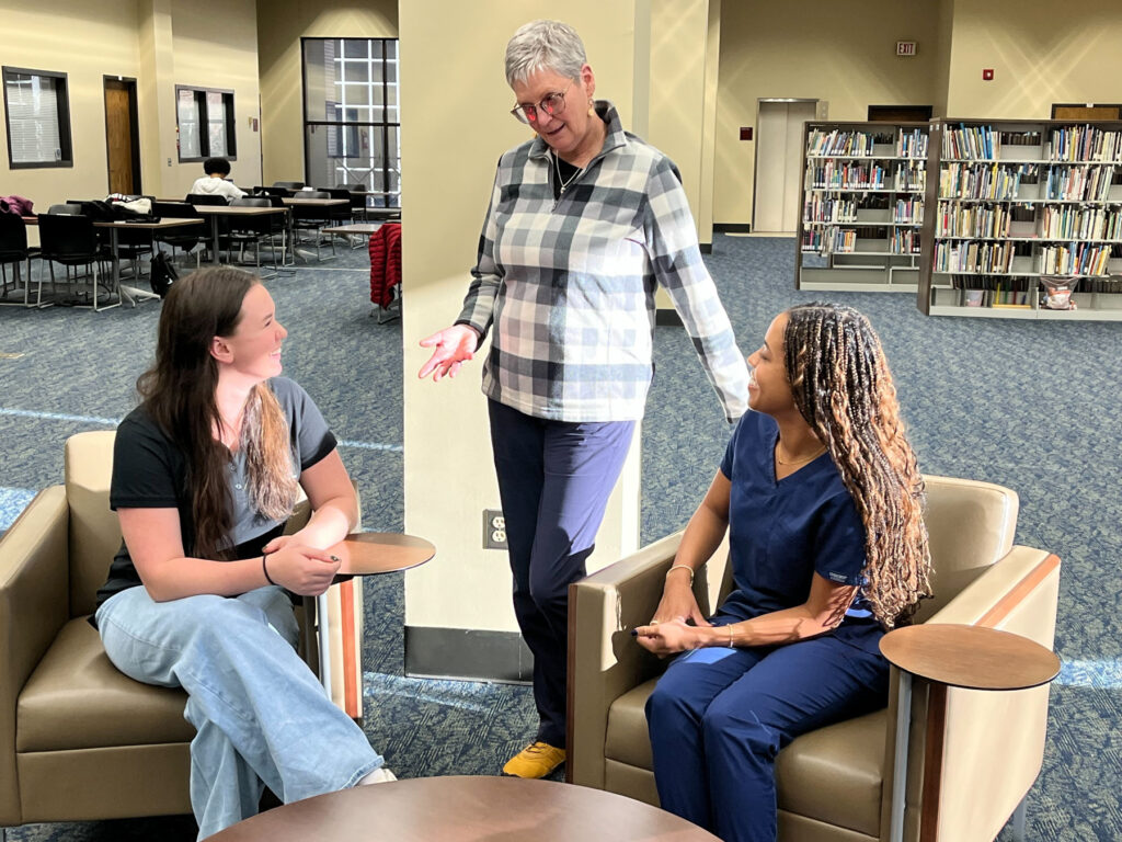 Emma Liz Soltay, Carol Bokros and Maya Henry talking in a library.