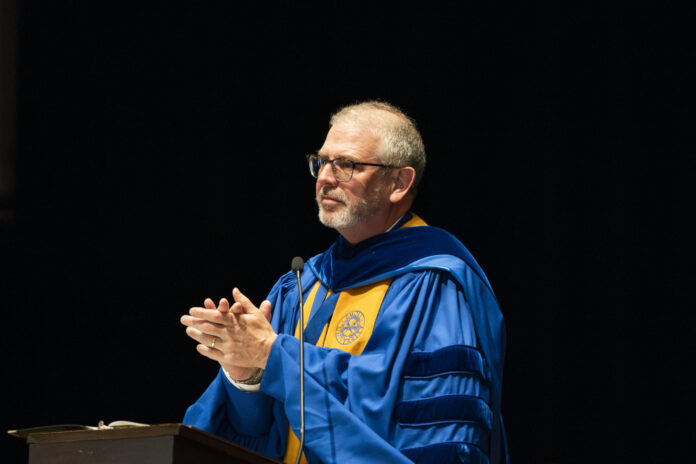 Dr. Scott Davis speaks at a podium against a dark background.