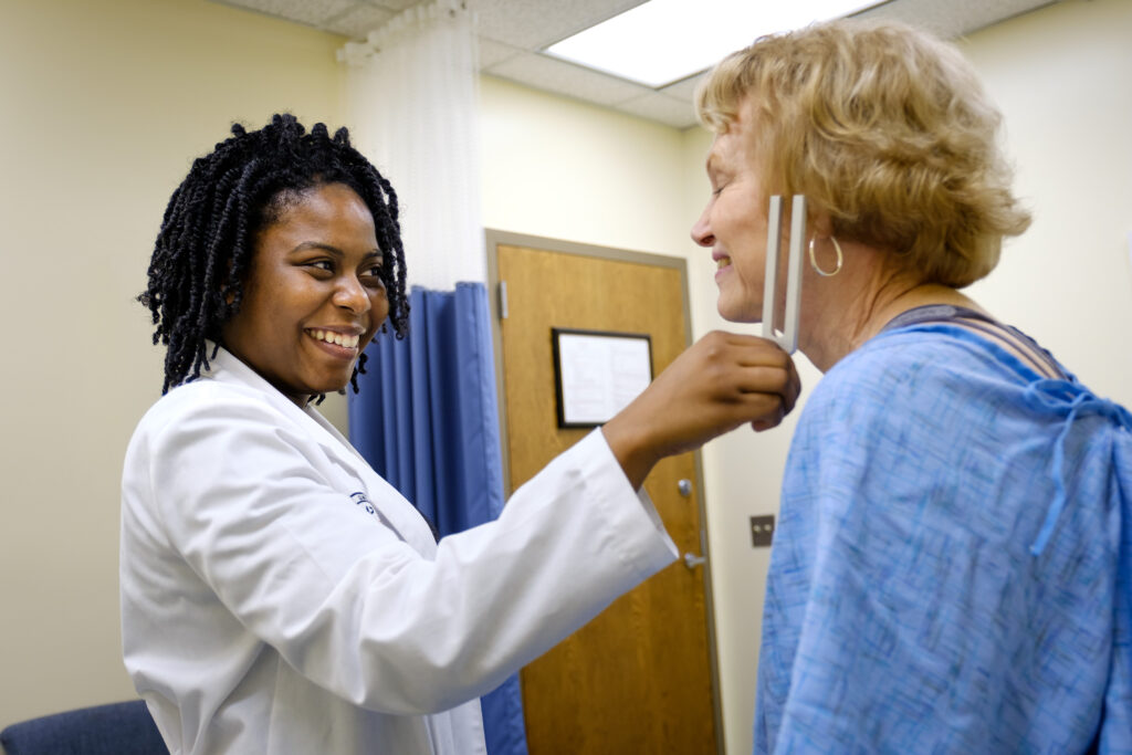 Medical student smiling while checking a patients neck with a medical instrument in a clinic room.