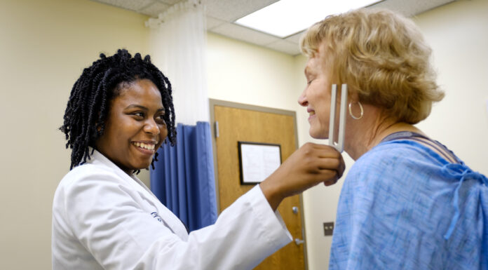 Mercer medical students get unique hands-on training in rural medicine Medical student smiling while checking a patients neck with a medical instrument in a clinic room.