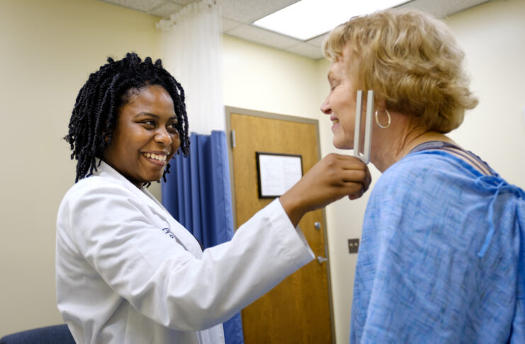 Medical student smiling while checking a patients neck with a medical instrument in a clinic room.