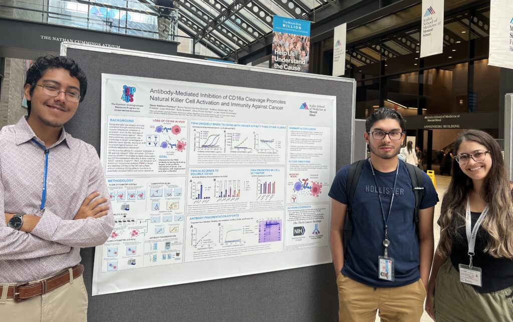 Three people stand in front of a scientific poster about immune response to cancer in an indoor exhibition space.