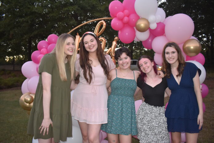 Phi Mu introductions event Five people smiling in front of a pink and white balloon arch outdoors.