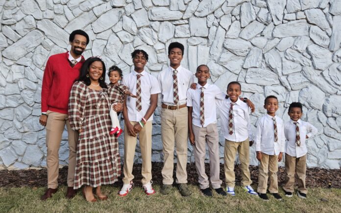 A family stands in front of a stone wall, wearing coordinated outfits with plaid patterns.