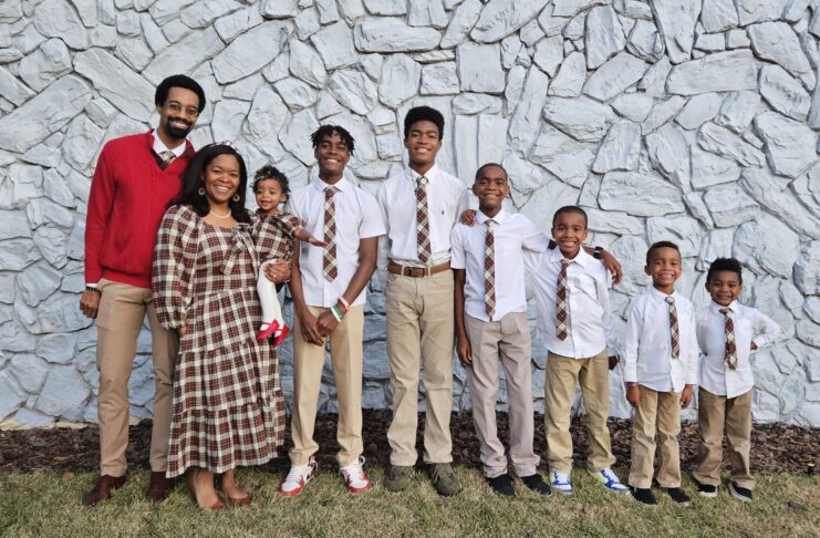 A family stands in front of a stone wall, wearing coordinated outfits with plaid patterns.