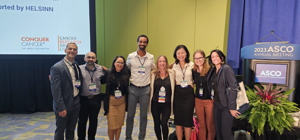 A group of eight people in professional attire stands together, smiling, at the ASCO 2023 Annual Meeting.