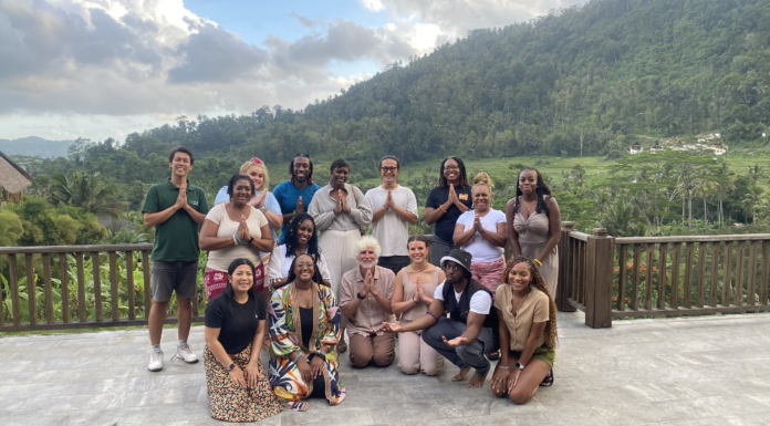 Exhibit highlights counseling students’ experiences in Bali A group of people poses outdoors on a patio with lush green hills and a cloudy sky in the background.