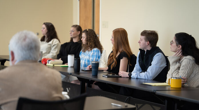 Externships serve critical role in experiential learning at Mercer Law A group of people seated at desks in a classroom, attentively listening to someone out of view.