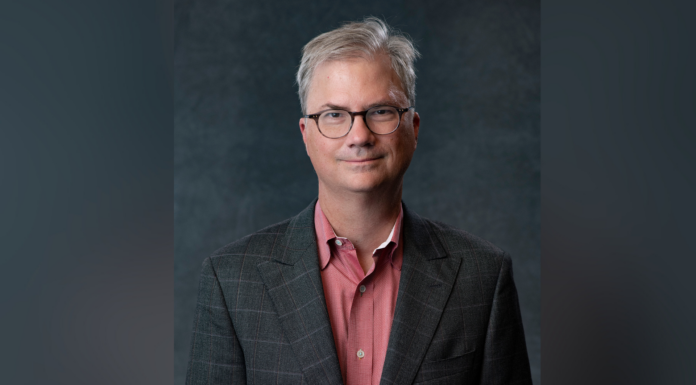 Accomplished scientist, research advocate Holden Thorp to deliver annual Lester Lectures Man with glasses in a plaid jacket and red shirt standing against a dark gray background.