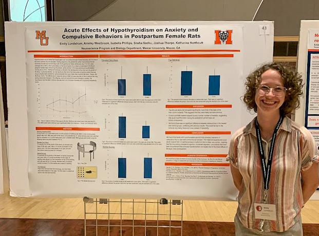 Person standing next to a scientific poster presentation on hypothyroidisms effects on rats, smiling at the camera.