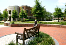 Underwood appointed as chancellor; trustees approve new student center construction Bronze sculpture of a person sitting on a bench in front of a brick building with circular architecture and green landscape.