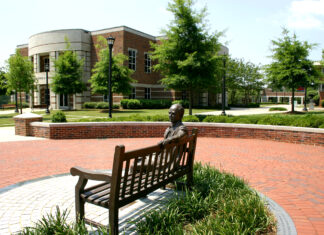 Underwood appointed as chancellor; trustees approve new student center construction Bronze sculpture of a person sitting on a bench in front of a brick building with circular architecture and green landscape.