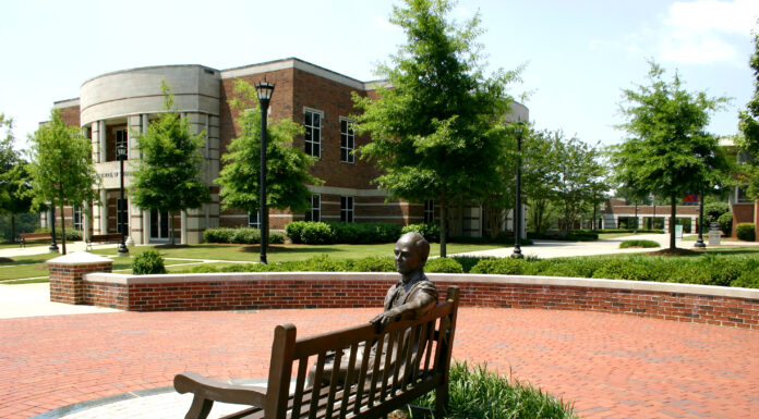 Get hands-on with science at Mercer’s “Science Spectacular” Bronze sculpture of a person sitting on a bench in front of a brick building with circular architecture and green landscape.