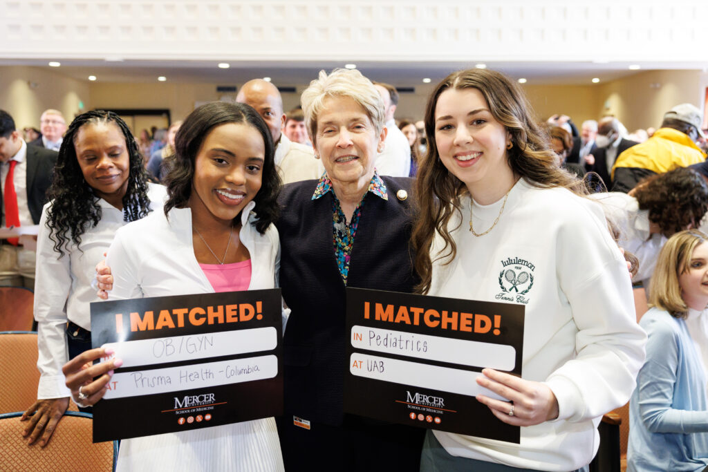 Three people standing together indoors, two holding I Matched! signs for OB/GYN and Pediatrics.
