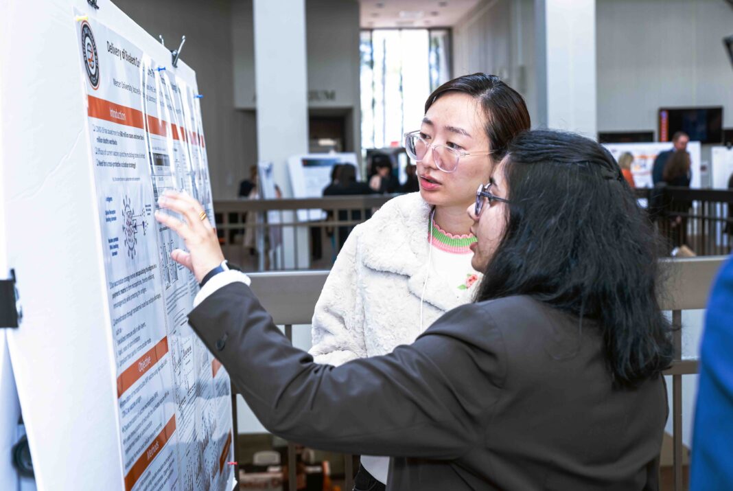 Two people discuss a scientific poster at a conference, one gesturing at the displayed information.