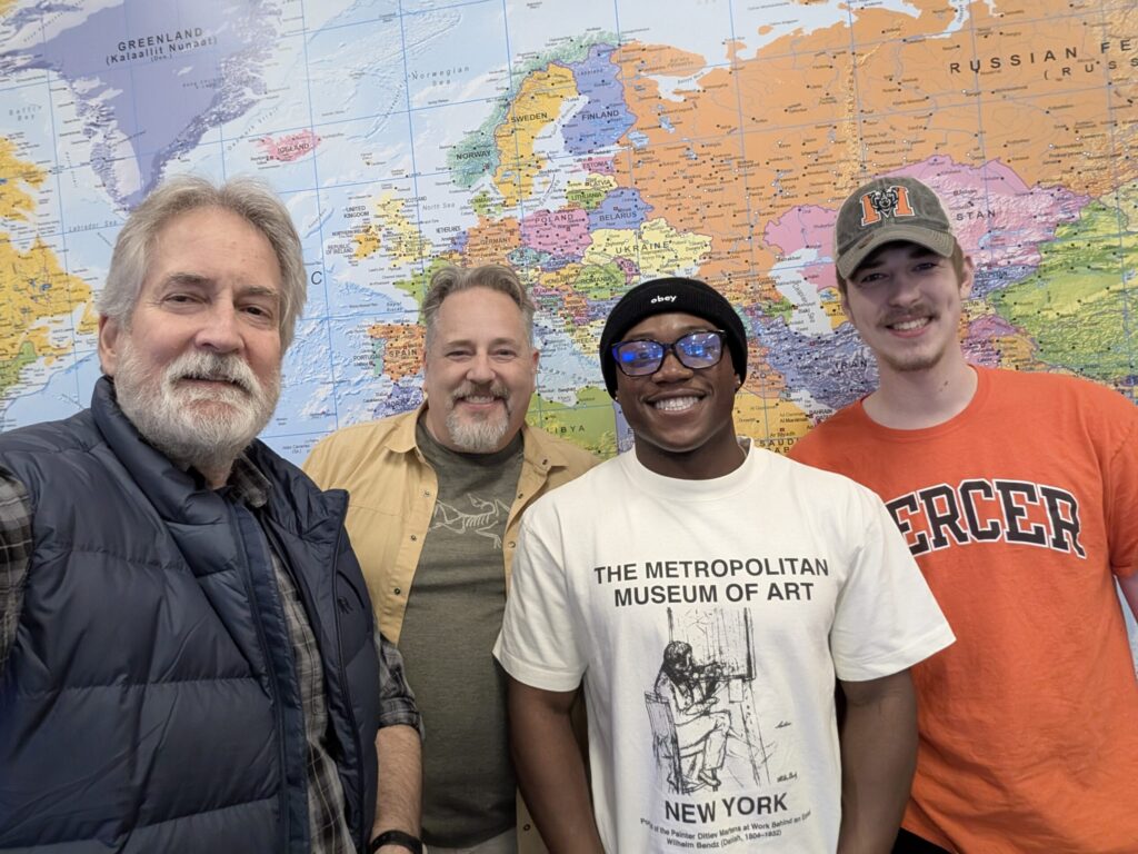 Four men stand smiling in front of a world map.
