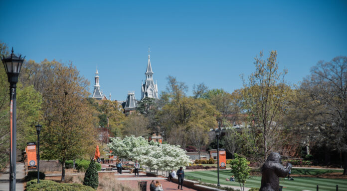 Faculty and Staff Notables | April 2025 A campus walkway with a bear statue, students walking, and spired buildings in the background under a clear blue sky.