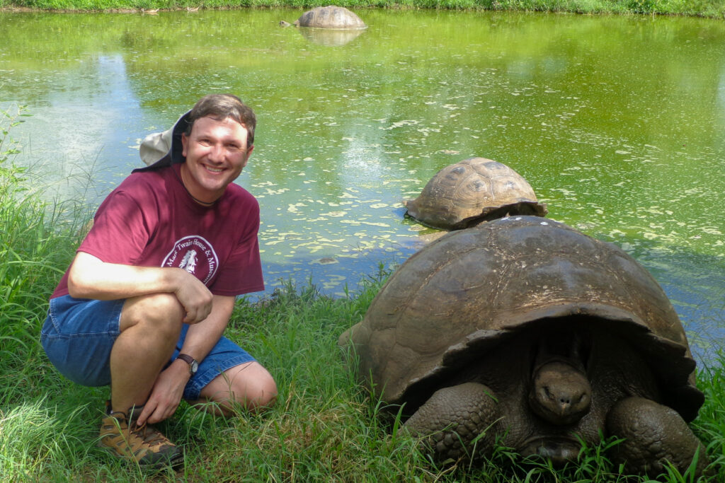 Brad Lindsey crouches beside a large tortoise in the Galapagos.
