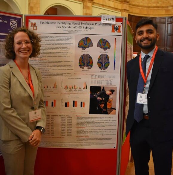 Two individuals stand beside a poster presentation on neural profiles in a large indoor venue.
