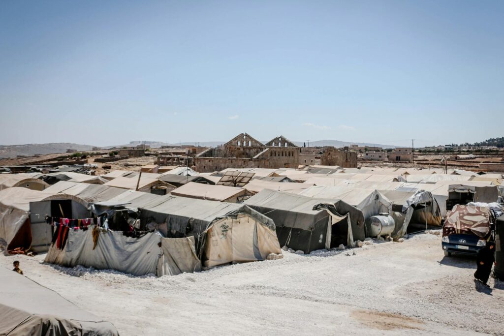 A wide view of a refugee camp with numerous tents arranged in rows, set on a barren landscape under a clear blue sky.