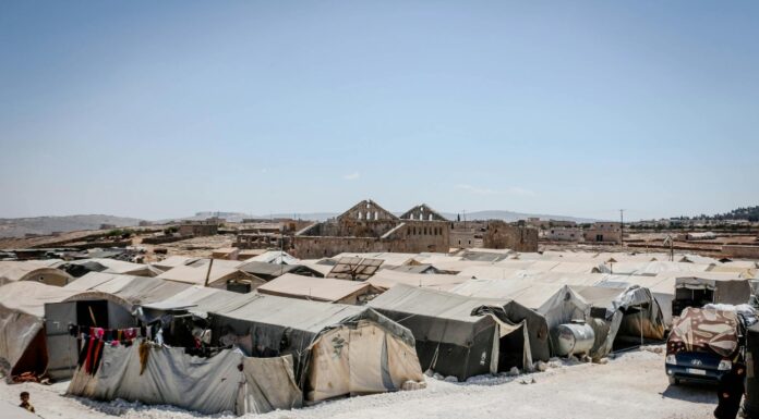 In a land of refugees, community will help you survive | Dr. Craig McMahan A wide view of a refugee camp with numerous tents arranged in rows, set on a barren landscape under a clear blue sky.