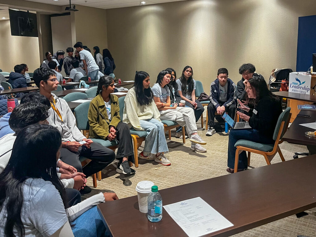 High school students sitting in a semi-circle listen to Dr. Katherine Perrotta speak