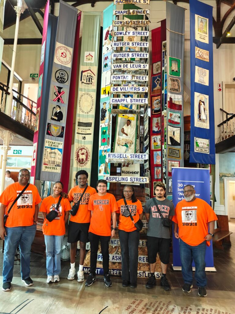 A group of people in orange shirts stand in front of a colorful display inside a museum.