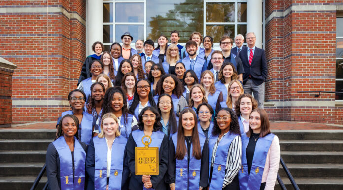College of Liberal Arts and Sciences inducts 46 students into Phi Beta Kappa Society A group of people, wearing blue stoles, pose on stairs in front of a brick building, holding a symbol and smiling.