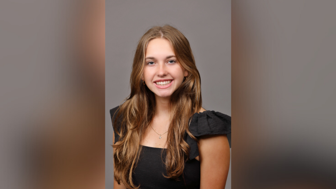 Smiling person with long hair wearing a black top against a neutral background.