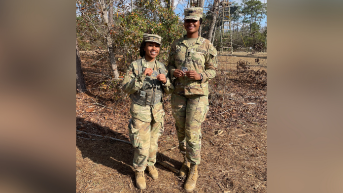 ROTC Two individuals in military uniforms stand outdoors on a forest path, each holding a small, round object.