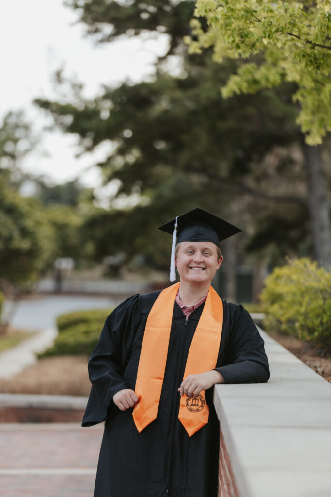 Dalton Loyd, in a graduation cap and gown, leans on a brick wall outdoors.