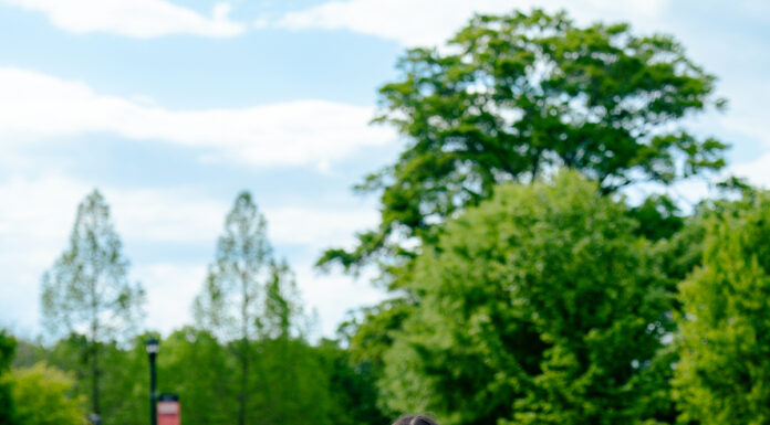 Graduate Spotlight: Jonalyn Hidalgo Jonalyn Hidalgo, in a white dress and orange graduation stole, holds a cap while standing outdoors on a paved walkway.