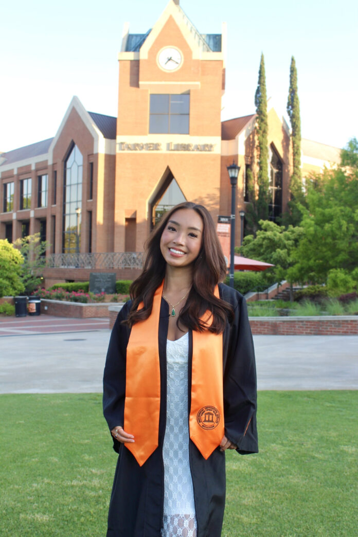 Linda Phan, in cap and gown stands, on Cruz Plaza.