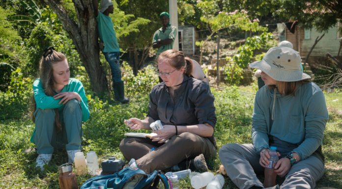Mercer professor makes engineering academy’s ‘40 Under 40’ list Three people sit on grass outdoors analyzing water samples with scientific equipment and bottles placed in front of them.