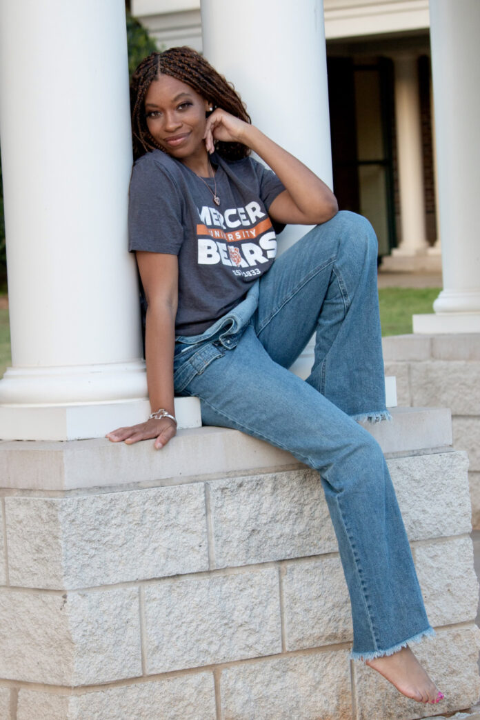 Quinecia Styles Smith in a Mercer University Bears shirt and jeans sits on a stone ledge in front of white columns.