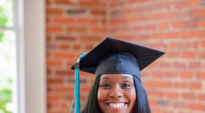 Graduate Spotlight: Tamia Sammons Tamia Sammons, in graduation attire, smiles while seated, holding an orange stole with a Mercer emblem.
