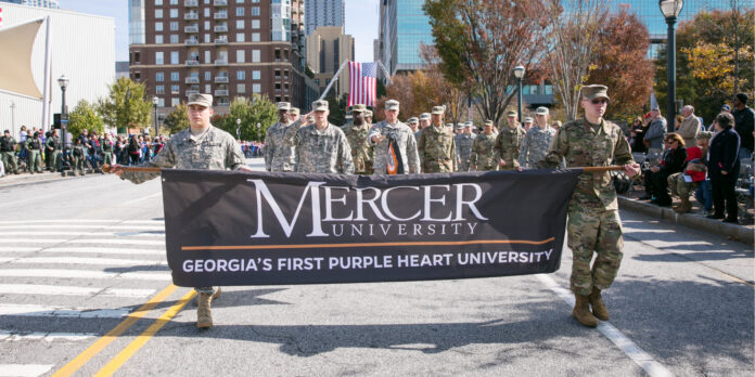 A group of people in military uniforms carrying a Mercer University banner during a street parade.