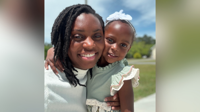 bre main 2 An adult and a young child smile outdoors, with the child wearing a white bow and green striped dress.